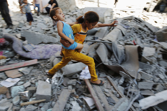 A Palestinian girl carries a child across rubble from a building that police said was destroyed by an Israeli air strike, in the Burij refugee camp in the central Gaza Strip August 1, 2014. (Reuters/Finbarr O'Reilly)
