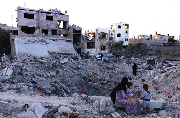 A Palestinian woman sits on August 11, 2014 with two boys at the edge of a crater left where her home used to be and which was completely demolished by an Israeli airstrike in Jabalia, northern Gaza Strip. (AFP Photo / Roberto Schmidt)