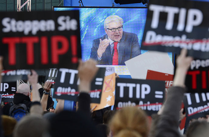 Protesters demonstrating against the Transatlantic Trade and Investment Partnership TTIP hold up signs in front of a screen showing German Foreign Minister Frank-Walter Steinmeier delivering a speech an election campaign meeting of the German Social Democratic Party for the upcoming European elections in Berlin, on May 19, 2014. (AFP Photo / John Macdougall)