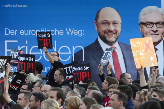 Protesters demonstrating against the Transatlantic Trade and Investment Partnership TTIP hold up signs in front of a placard picturing German Foreign Minister Frank-Walter Steinmeier (R) and Top candidate of the German Social Democratic Party (SPD) for the 2014 European elections Martin Schulz during an election campaign meeting of the German Social Democratic Party for the upcoming European elections in Berlin, on May 19, 2014. (AFP Photo)