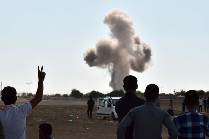 A Kurdish man flashes the V-sign for victory as smoke rises following an air strike on the western sector of the Syrian town of Ain al-Arab, known as Kobane by the Kurds, as seen from the Turkish-Syrian border, in the southeastern town of Suruc, Sanliurfa province, on October 8, 2014. (AFP Photo / Aris Messinis)