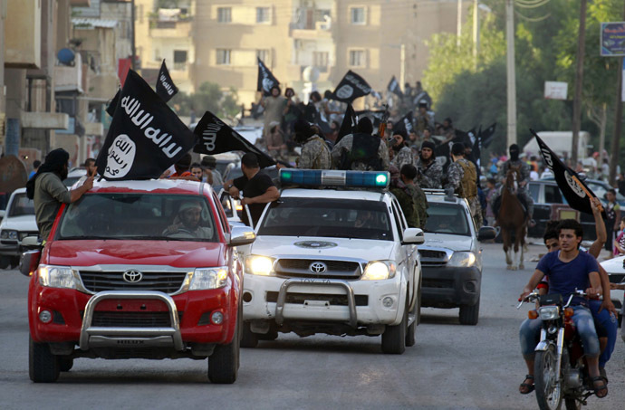 Militant Islamist fighters waving flags, travel in vehicles as they take part in a military parade along the streets of Syria's northern Raqqa province, June 30, 2014 (Reuters)