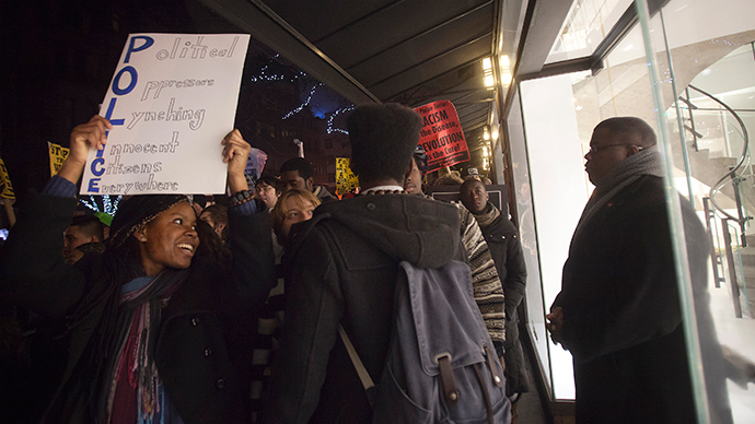 A protester holding a sign passes by a luxury store guarded by a security officer as fellow protesters walk up Madison Ave during a demonstration against the police in the Manhattan borough of New York December 23, 2014 (Reuters / Carlo Allegri)