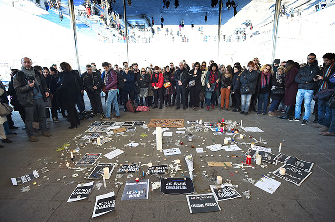 People gather next to signs reading ''I am Charlie'' and candles placed on the ground, after observing a minute of silence in the old Harbor in Marseille on January 8, 2015 for the victims of an attack by armed gunmen on the offices of French satirical newspaper Charlie Hebdo in Paris on January 7 which left 12 people dead. (AFP Photo/Anne-Christine Poujoulat)