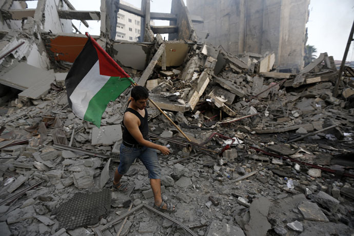 A Palestinian resident carries a national flag as he inspects the remains of Al-Basha, a building that was destroyed by an Israeli air strike in Gaza City (AFP Photo)