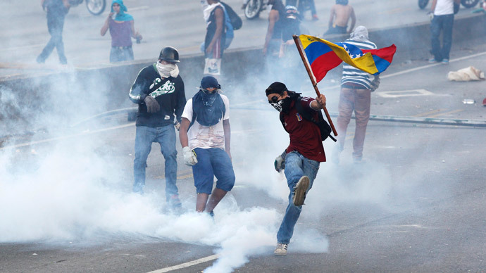 An anti-government protester, with the Venezuelan flag, kicks back a gas canister to police during a demonstration in which masked youths battled police and blocked a main highway in Caracas.(Reuters / Christian Veron)