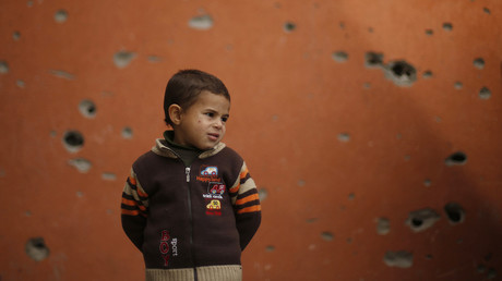 Enfant palestinien se tenant devant un batiment endommagé à Gaza
