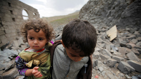 11 août 2016 : un garçon porte sa sœur en marchant sur les décombres d'une maison détruite par une frappe aérienne saoudienne dans la capitale du Yémen Sanaa