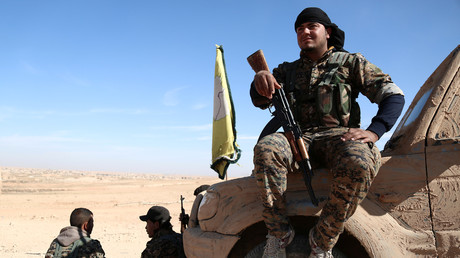 Un combattant des Forces démocratiques syriennes patiente armé sur un véhicule camouflé à l'aide de boue.