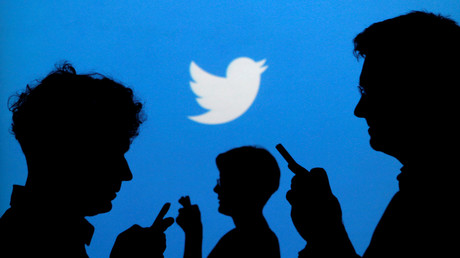 Des silhouettes d'utilisateurs de smartphones devant le logo de Twitter