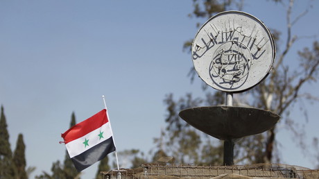 Un drapeau de la République arabe syrienne à côté d'un emblème de l'Etat islamique 
