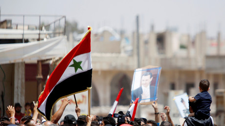 Des Syriens arborent le drapeau de leur pays ainsi qu'un portrait du président Bachar el-Assad à Deraa, le 4 juillet 2018 (image d'illustration).