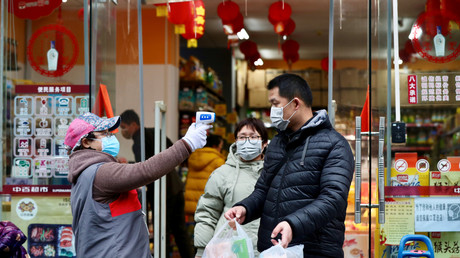 Une personne prend la température de clients qui sortent d'un supermarché, le 7 février à Wuhan, en Chine.