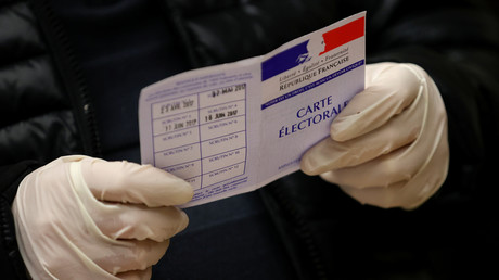 Un fonctionnaire, portant des gants en latex, tient une carte d'électeur dans un bureau de vote lors du premier tour des élections municipales à Strasbourg, le 15 mars 2020.