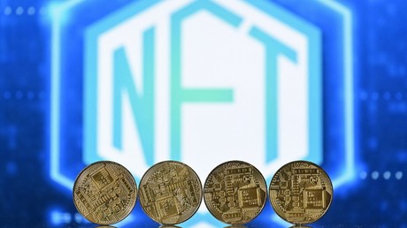 Une photo d'illustration prise à Londres le 30 décembre 2021 montre des pièces de crypto-monnaie disposées devant un écran affichant un logo NFT.