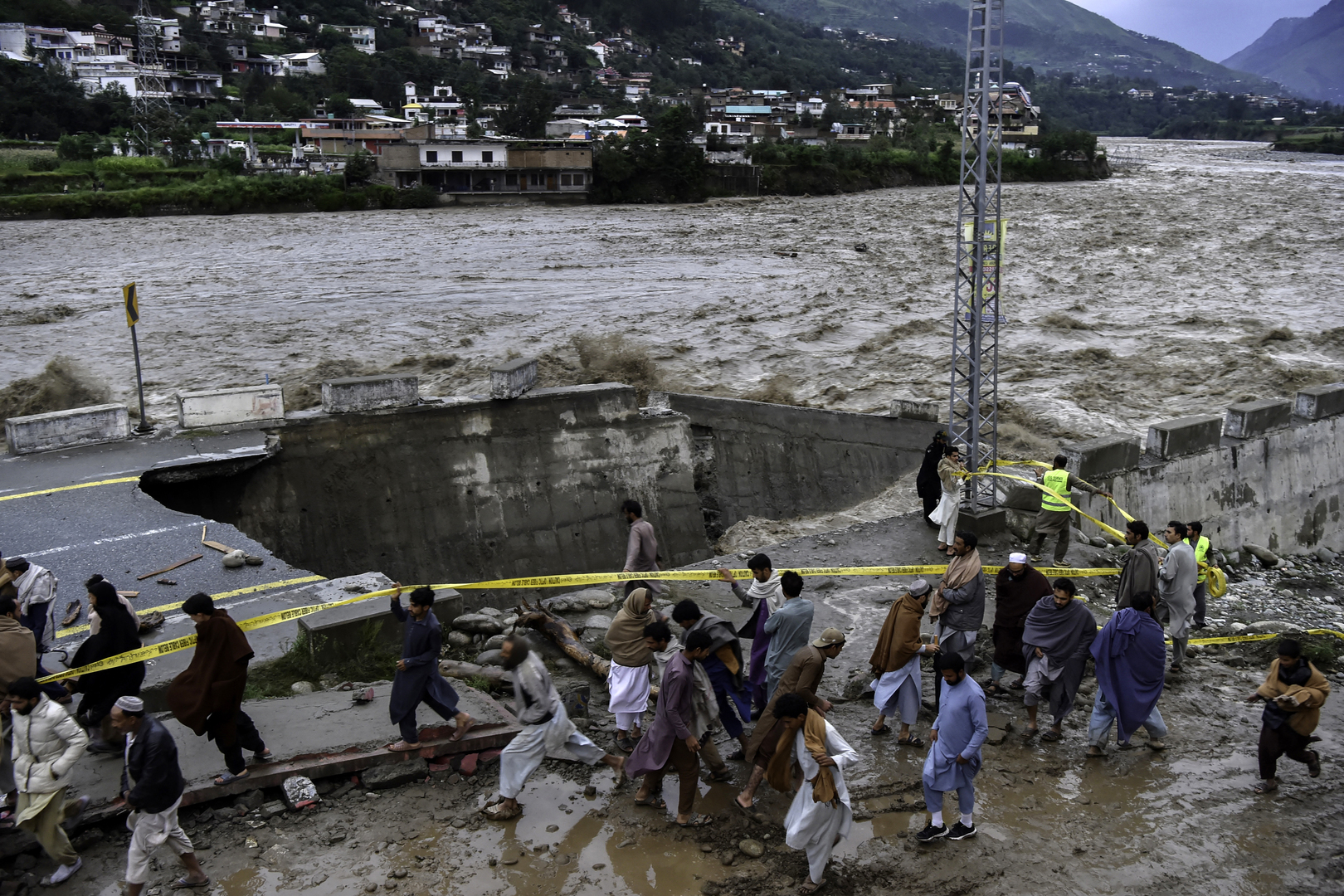Des personnes se rassemblent devant une route endommagée par les eaux de crue suite aux fortes pluies de mousson dans la région de Madian, dans la vallée de Swat, au nord du Pakistan, le 27 août 2022.