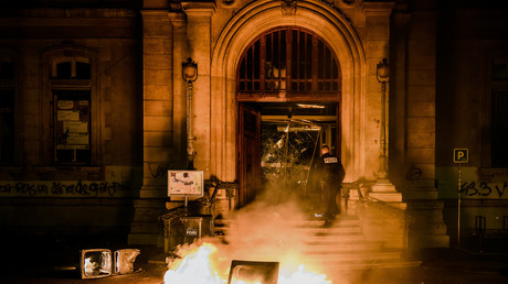 Un policier tente d'éteindre les flammes à l'entrée de la mairie du IVe arrondissement de Lyon dans la nuit du 17 au 18 mars 2023.