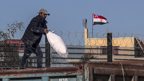 Un employé jette un sac humanitaire par-dessus les barrières à Gaza à la frontière égyptienne.