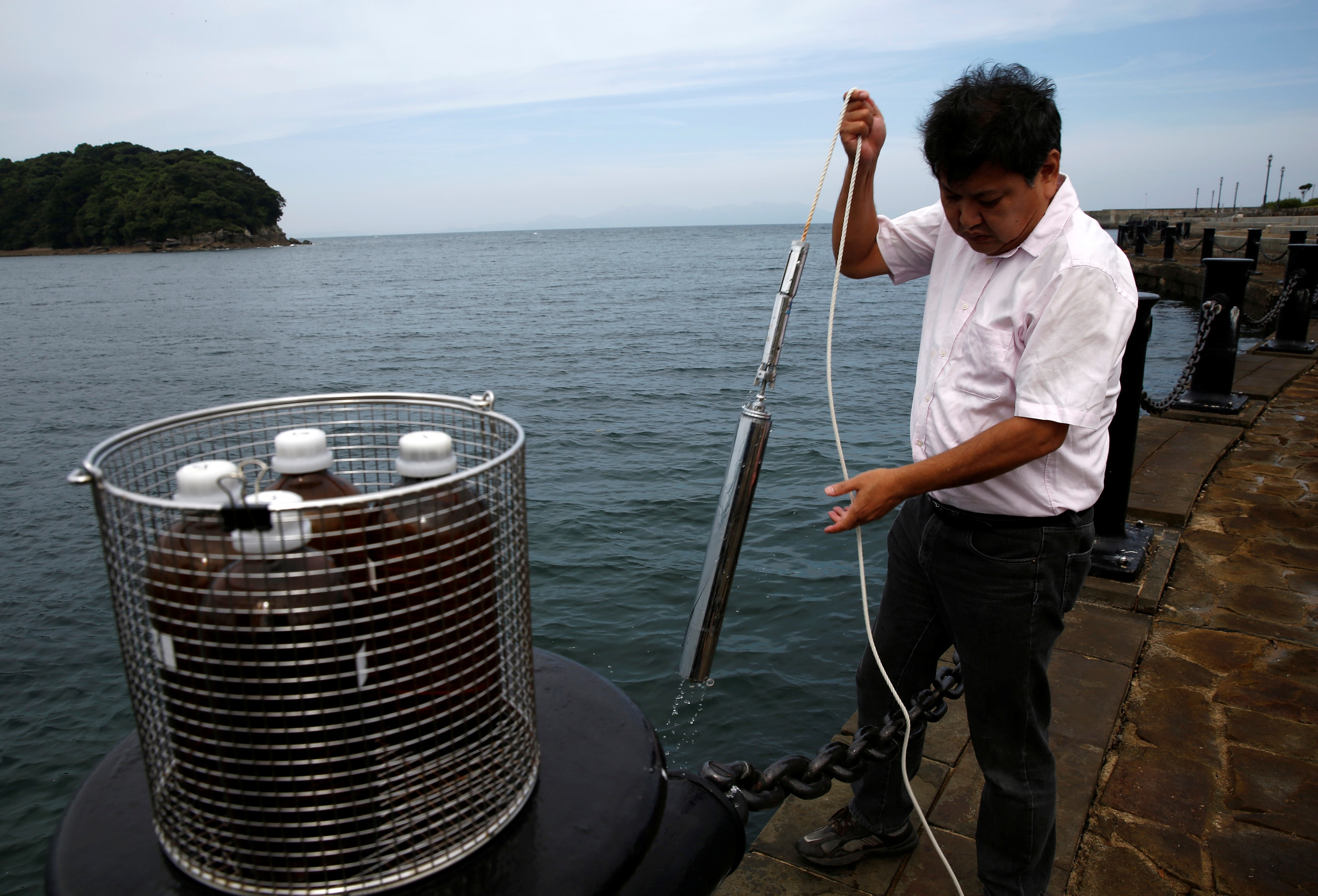 Инженер из Национального института Минамата собирает образцы воды из залива
