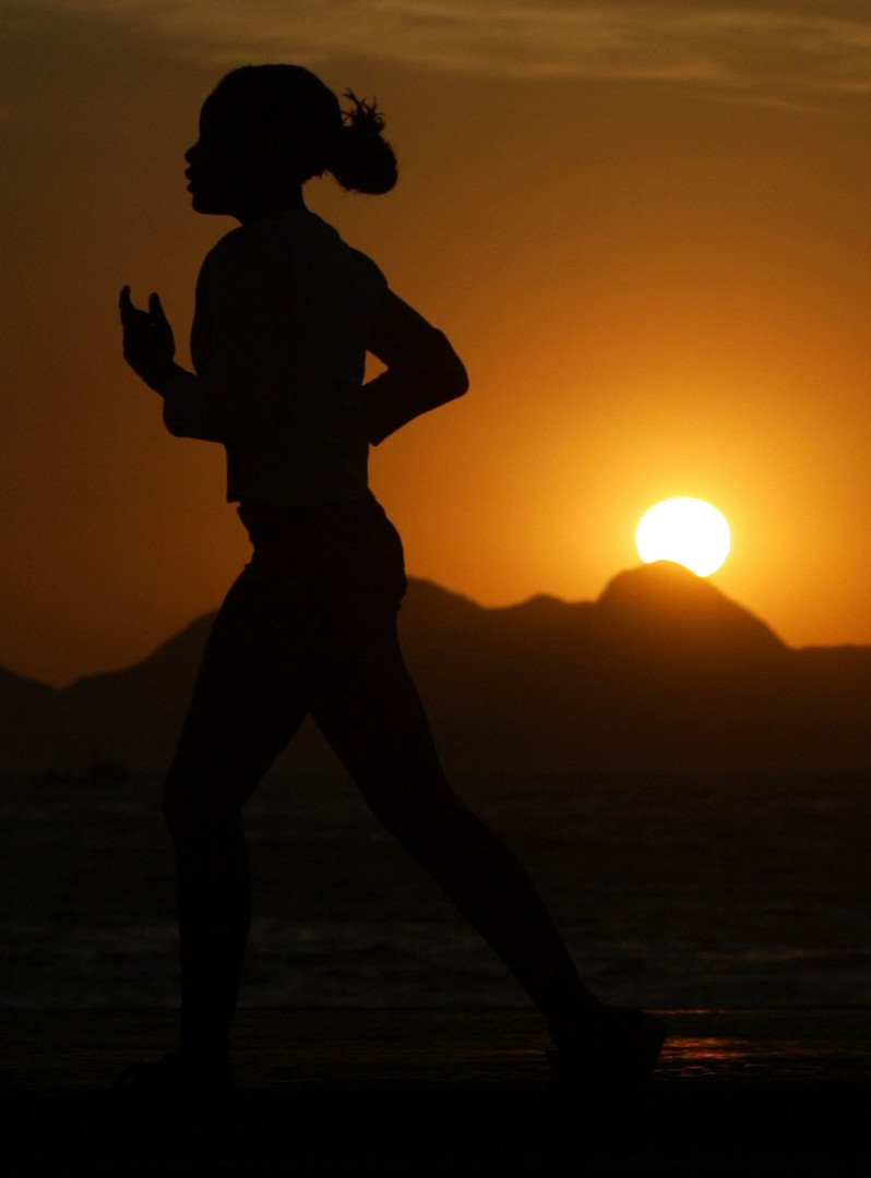 امرأة تركض للتمتع بنسيم البحر على شاطئ كوبا كابانا مع شروق الشمس، ريو دي جانيرو، البرازيل، 15/سبتمبر
