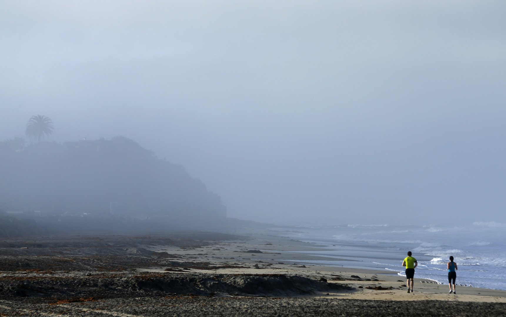  رجل وامرأة يتمتعان بنسيم البحر أثناء ممارسة رياضة الجري على شاطئ كارديف، كاليفورنيا، 17 مارس/آذار 