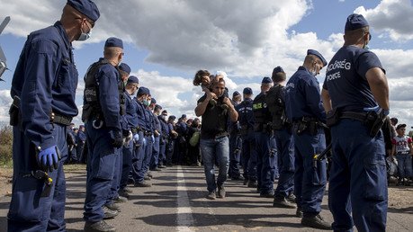 مهاجر يحمل طفله ماشيا بين صفين من رجال الشرطة متجها إلى حافلة تقف في نقطة التجمع بالقرب من قرية روجكي الهنغارية