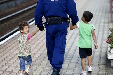 رجل من الشرطة يرافق طفلين مهاجرين طوال رصيف يؤدي إلى قطار متجه إلى ميونيخ من محطة قطار في هنغاريا