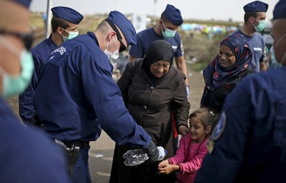 رجال من الشرطة الهنغارية يرافقون مهاجرين ينتظرون وقت ركوب حافلة في نقطة التجمع للمهاجرين بالقرب من الحدود الهنغارية الصربية