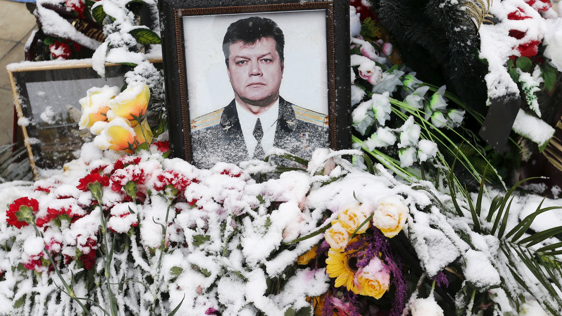 أزهار مغطاة بالثلج أمام صورة لأوليغ بيشكوف طيار القاذفة الروسية التي أسقطت في سوريا