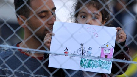 فتاة صغيرة من المهاجرين في مخيم مسيج تمسك ورقة عليها رسم 