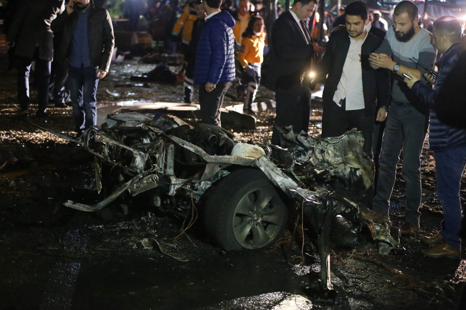 رجال من الأجهزة الأمنية ومارة يقفون بجانب ما تبقى من السيارة الملغمة بعد تفجيرها