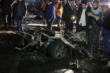 رجال من الأجهزة الأمنية ومارة يقفون بجانب ما تبقى من السيارة الملغمة بعد تفجيرها