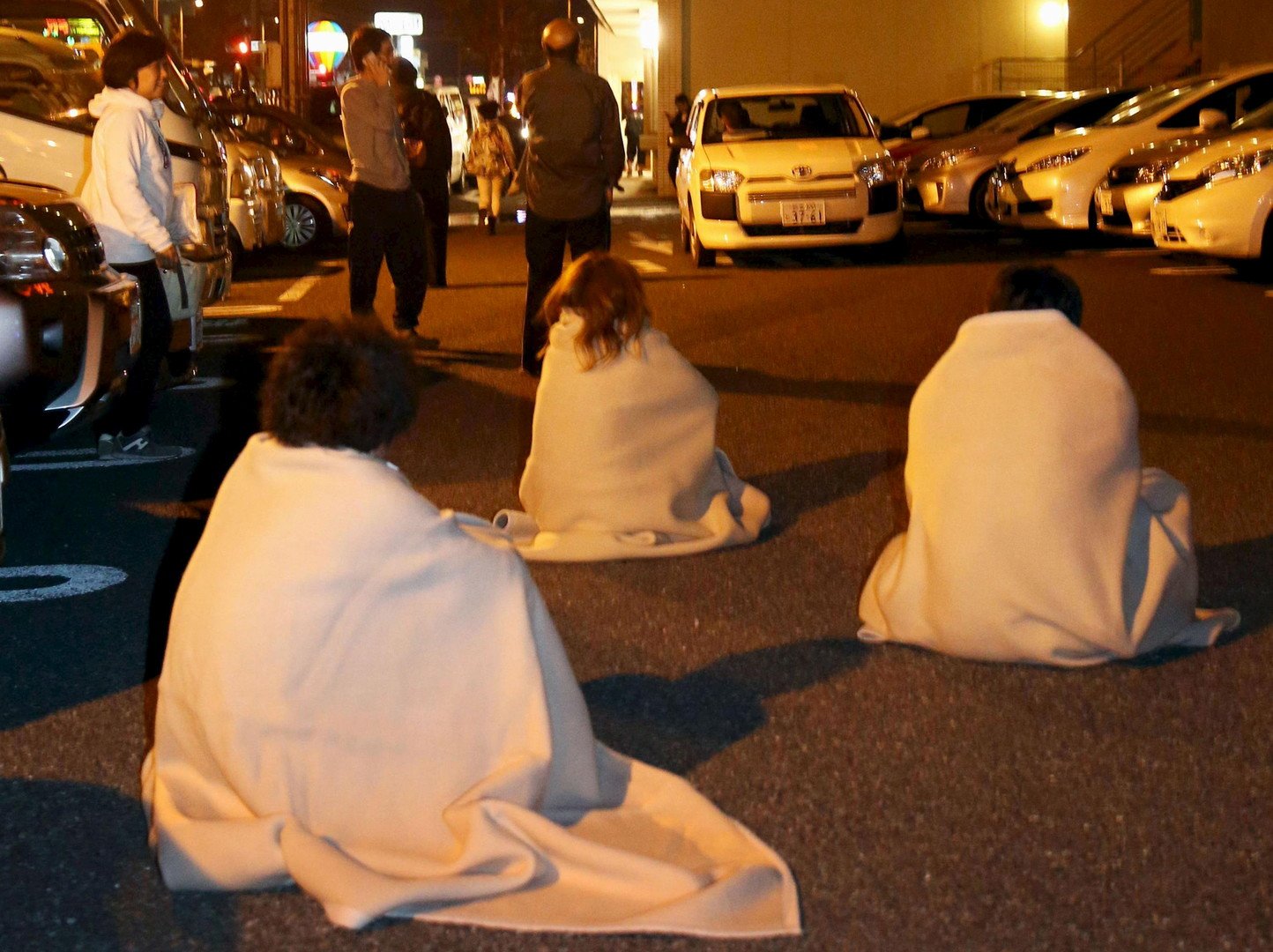 متضررون من الزلزال متلففون بالبطانيات يجلسون على الطريق بعد إجلائهم من فندق بعد وقوع الزلزال في كوماموتو بجنوب اليابان.