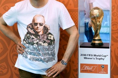 رجل يلبس قميصا عليه صورة الرئيس الروسي فلاديمير بوتين وهو يقف على خلفية كأس بطولة العالم لعام 2018