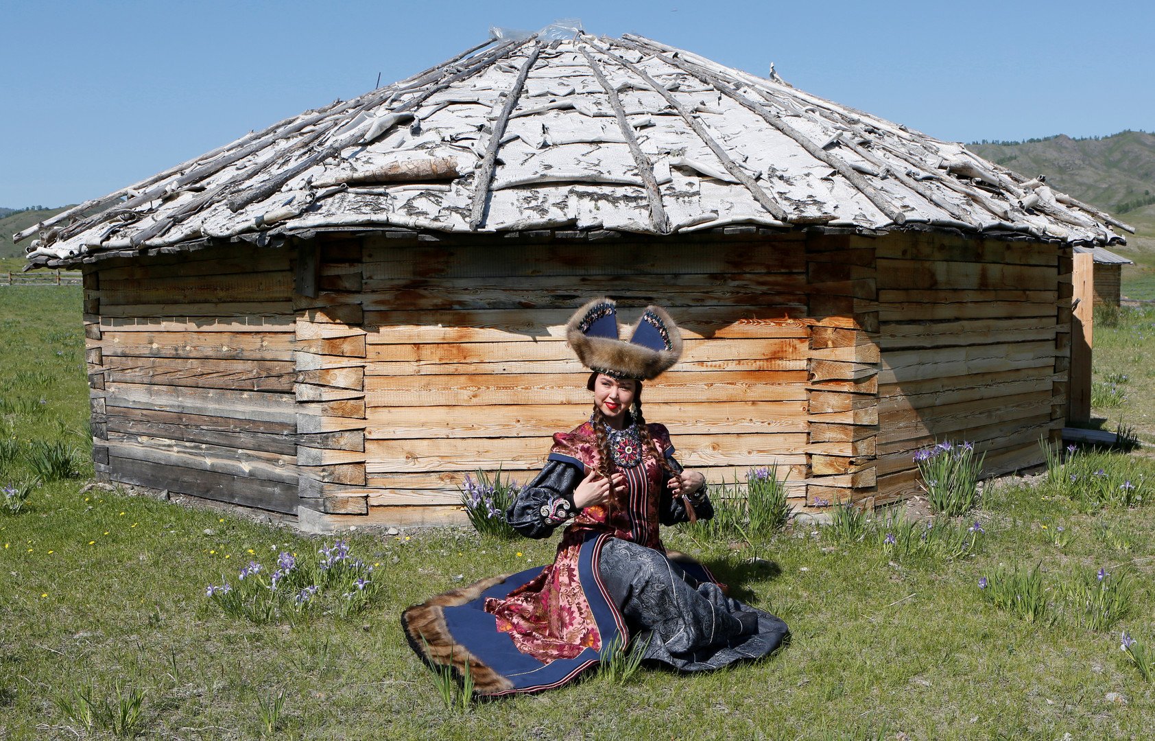 عارضة من مسرح الموضة الخكاسية تقدم زيا تقليديا في أثناء بروفة "عيد الحليب الأول" وذلك على خلفية كوخ من المتحف الإثني