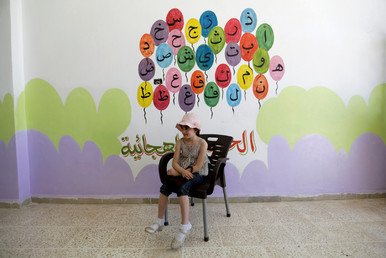 طالبة مدرسة تجلس بجانب جدار مزخرف بأحرف الأبجدية العربية