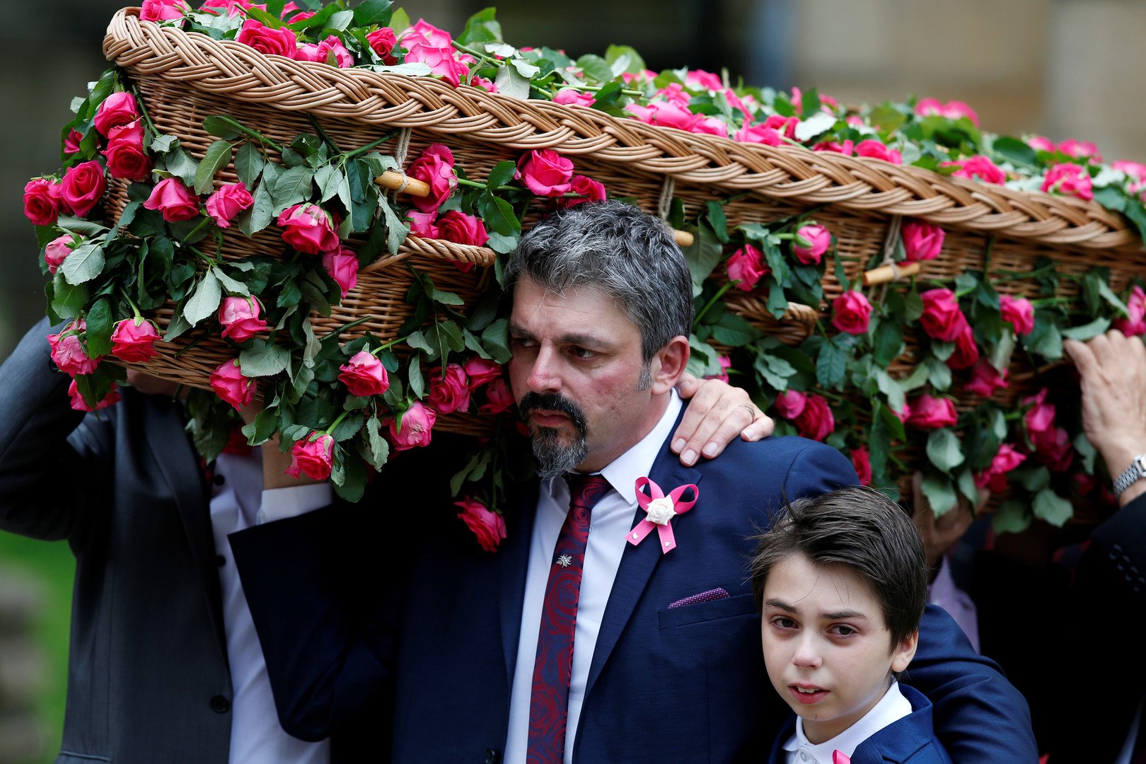 أندرو روز روسوس يضم ابنه بيد، ويحمل بالأخرى تابوت ابنته صافي روز روسوس، أصغر ضحية في هجوم ساحة مانشستر، في الجنازة المقامة بكاتدرائية مانشستر. 26 يوليو 2017