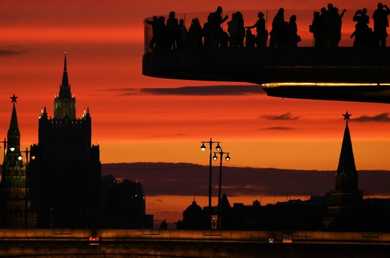 زوار وسياح على الجسر الطائر (بورياشيي موست) في حديقة زارياديه وسط مدينة موسكو، وعلى خلفيته: أبراج الكرملين ومبنى وزارة الخارجية الروسية