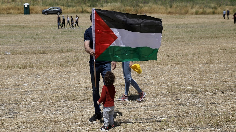 طفلة تقف أمام العلم الفلسطيني
