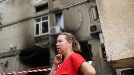 مستوطِنة في عسقلان أمام بناية متضررة بصواريخ المقاومة الفلسطينية