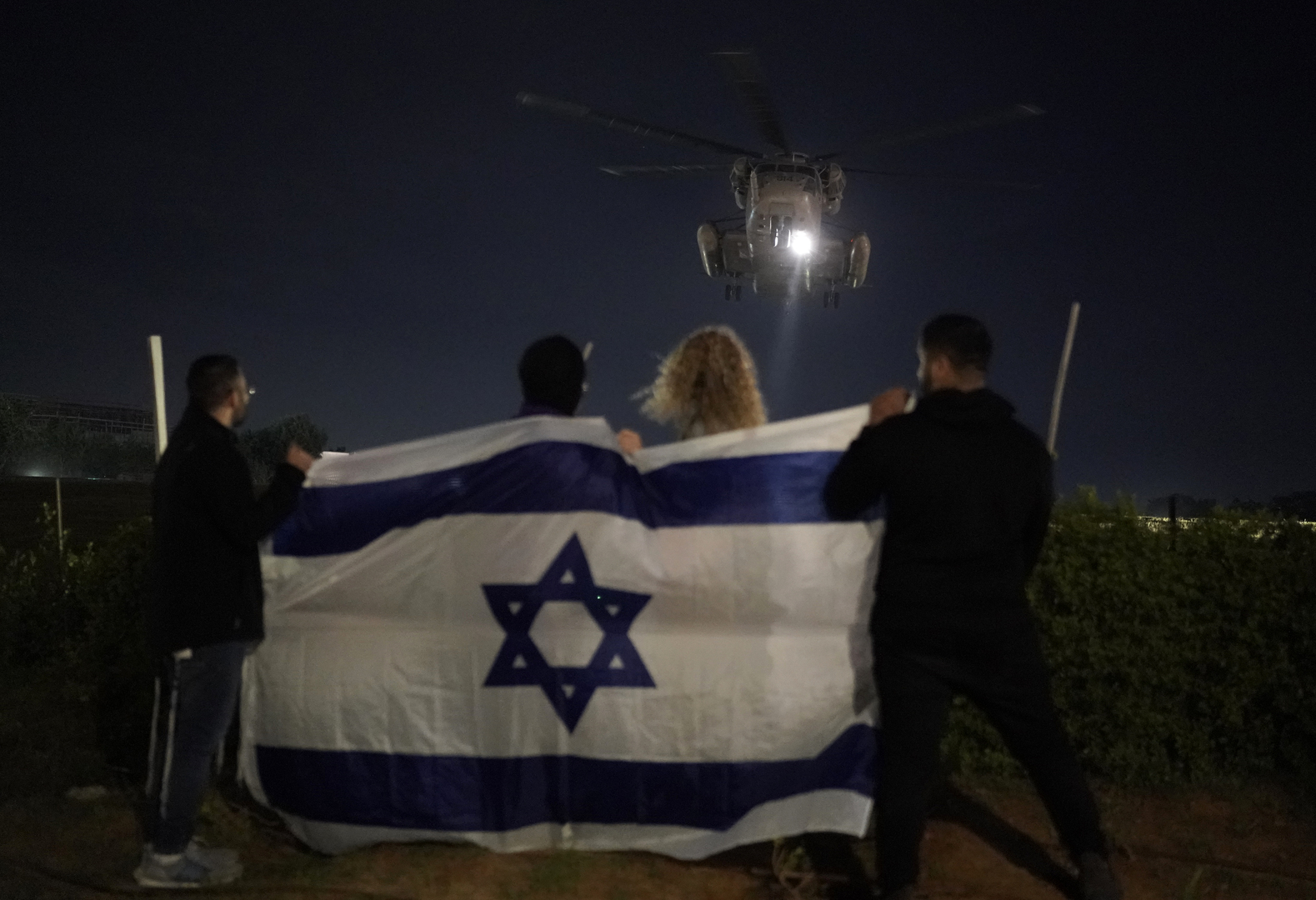 أشخاص يحملون العلم الإسرائيلي يشاهدون وصول مروحية تنقل رهائن إسرائيليين أفرجت عنهم حماس في مركز شيبا الطبي في رمات غان