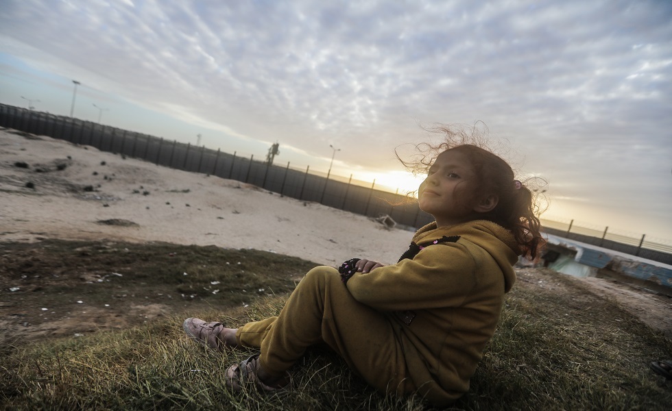 طفلة فلسطينية نازحة من شمال غزة تجلس قرب الجدار الفاصل بين مصر والقطاع
