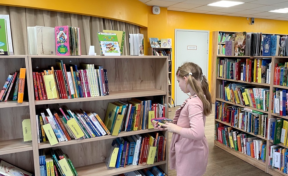 طفلة تقف أمام رفوف كتب باللغة الروسية