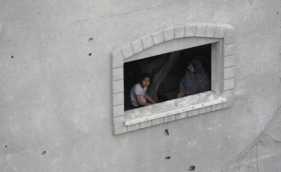 سيدة فلسطينية مع فتاة أمام نافذة منزل أصيب بنيران إسرائيلية في مخيم النصيرات للاجئين - جنوب قطاع غزة.