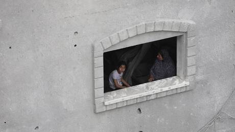 سيدة فلسطينية مع فتاة أمام نافذة منزل أصيب بنيران إسرائيلية في مخيم النصيرات للاجئين - جنوب قطاع غزة.