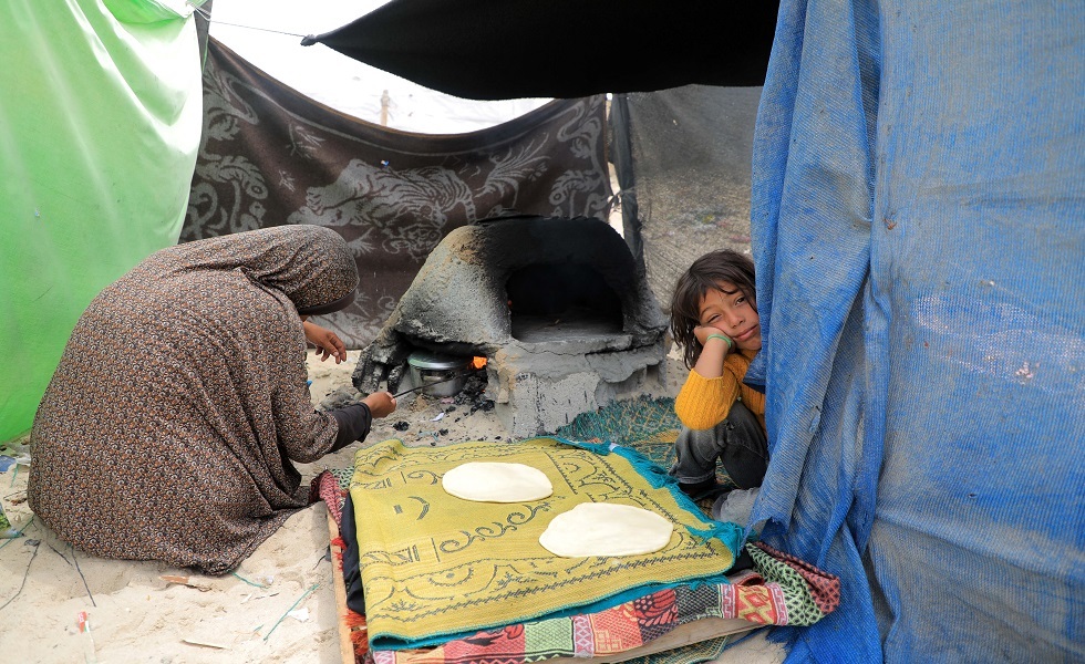 سيدة فلسطينية تم إجلاؤها من رفح تقوم بإعداد الطعام على شاطئ في خان يونس جنوب قطاع غزة- مايو 2024