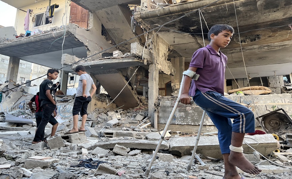 صبي على عكازين بينما يتفقد الفلسطينيون مبنى تعرض لقصف إسرائيلي في رفح جنوبD قطاع غزة - مايو 2024