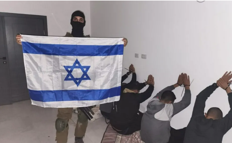 جندي إسرائيلي ينشر صورة لمعتقلين في الضفة الغربية وهو يحمل العلم الإسرائيلي.