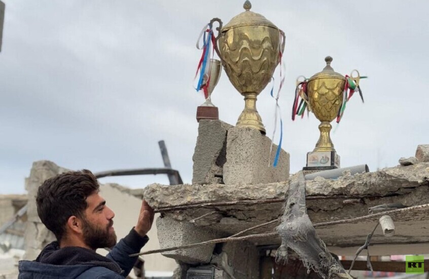 في مشهد مؤثر..  لاعب فلسطيني يضع كؤوس انتصاراته فوق ركام منزله المهدم