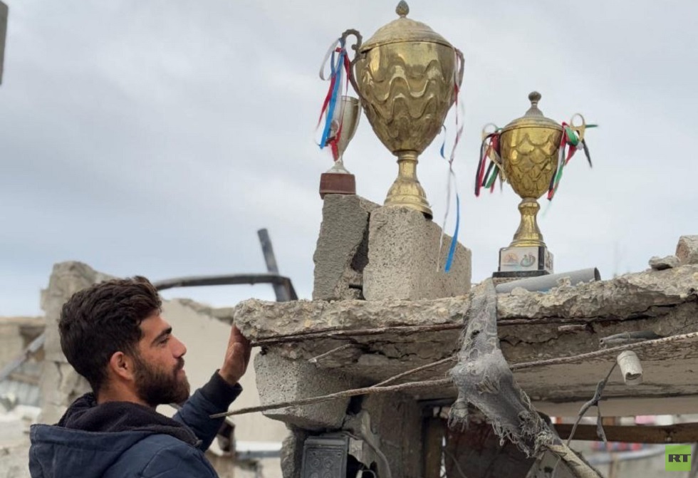 في مشهد مؤثر.. لاعب فلسطيني يضع كؤوس انتصاراته فوق ركام منزله المهدم